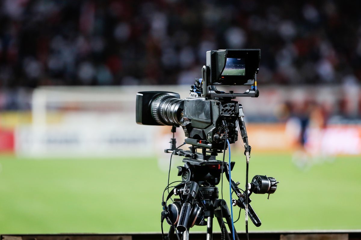 The Streamline logo over a broadcast camera on a tripod at the edge of the pitch